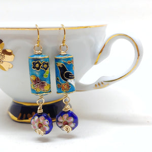 Gold dangly cloisonné bauble earrings featuring vibrant blues with butterfly, birds, and daisy motifs.