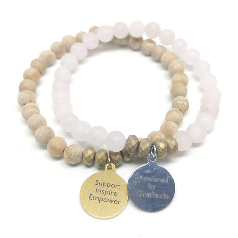 Mother's Day Charm Bracelet Bundle featuring matte rose quartz bracelet and stainless steel "Powered By Gratitude" charm, and silk wood bracelet featuring brass "Support, Inspire, Empower" charm.  Stretch Bracelets.